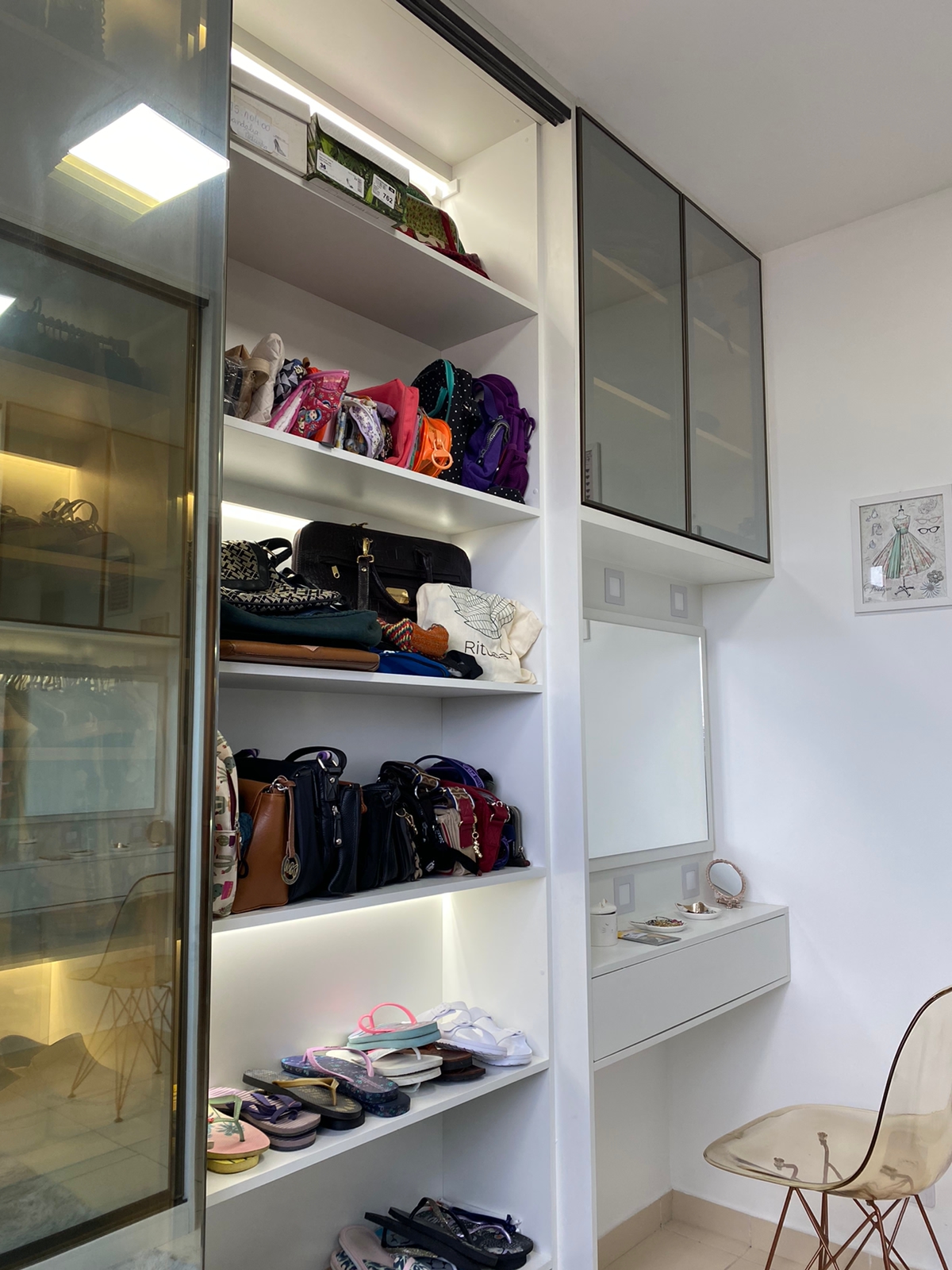 Closet planejado branco com prateleiras abertas para bolsas e calçados, portas de vidro fumê e iluminação LED